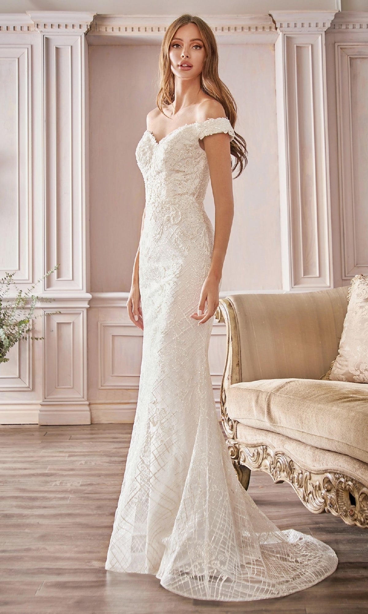 A woman in the Ladivine CD929 Long Off-White Wedding Dress stands beside a beige upholstered sofa in an elegant, light-paneled room.